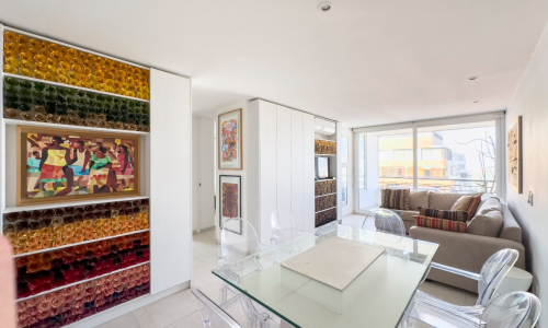 Living comedor moderno con decoración artística, mesa de vidrio y sofá frente a gran ventanal